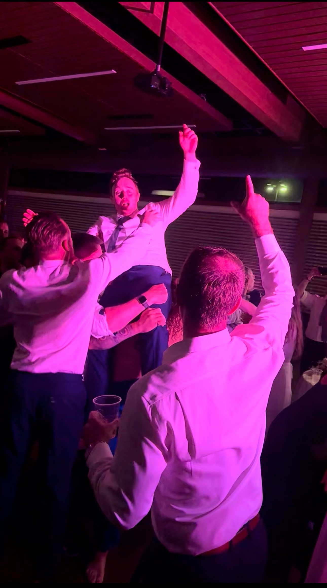 A professional wedding DJ in Fort Wayne, Indiana, mixing music at a lively wedding reception, with guests dancing and colorful lights illuminating the dance floor.